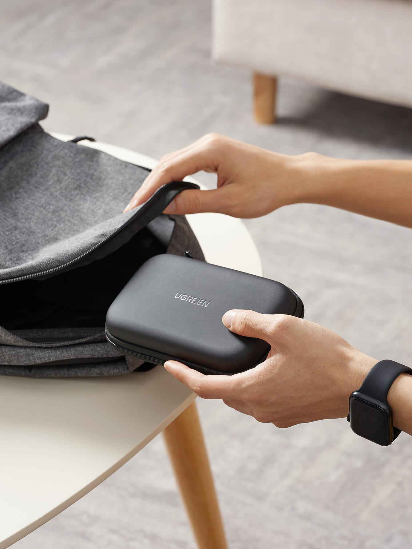 Hände legen einen schwarzen Koffer aus einer grauen Tasche auf einen weißen Tisch.