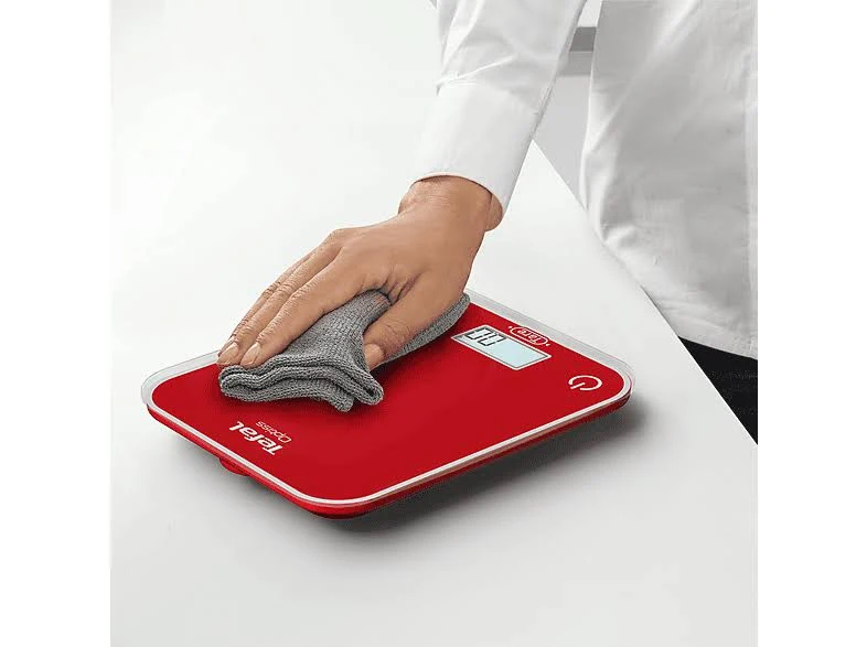 Una báscula de cocina digital roja con un paño gris encima. Una mano limpia la báscula.