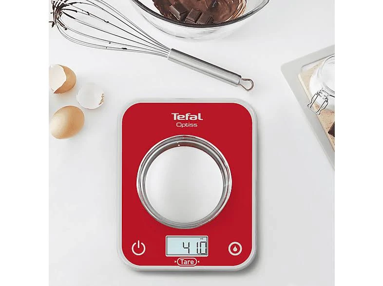 Báscula de cocina digital Tefal Optiss roja con azúcar y un batidor sobre una superficie blanca.