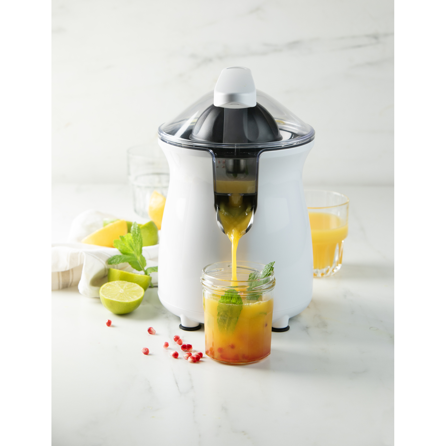 A white juicer with a clear lid, pouring orange juice into a glass with mint.