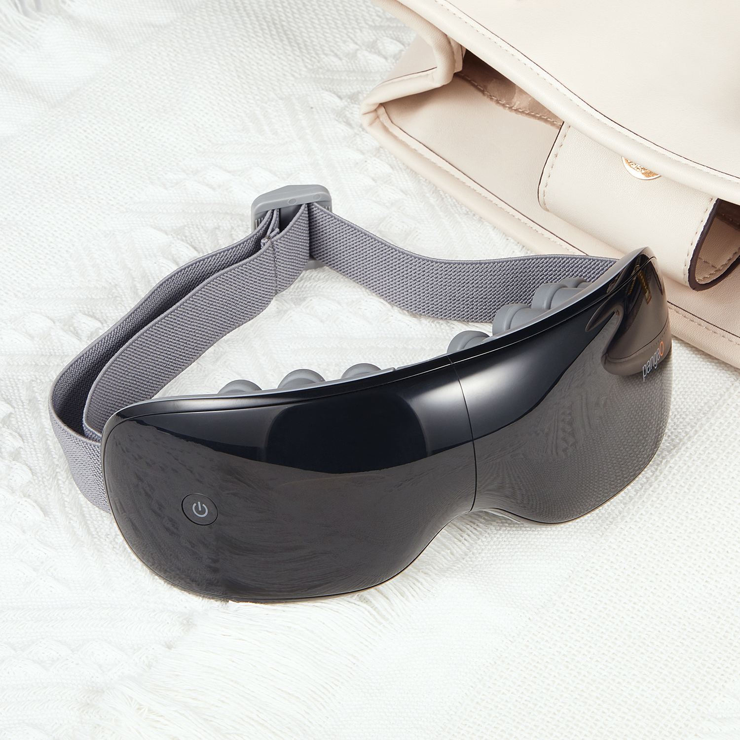 Black eye massager on a white blanket. Has a power button and brand logo.