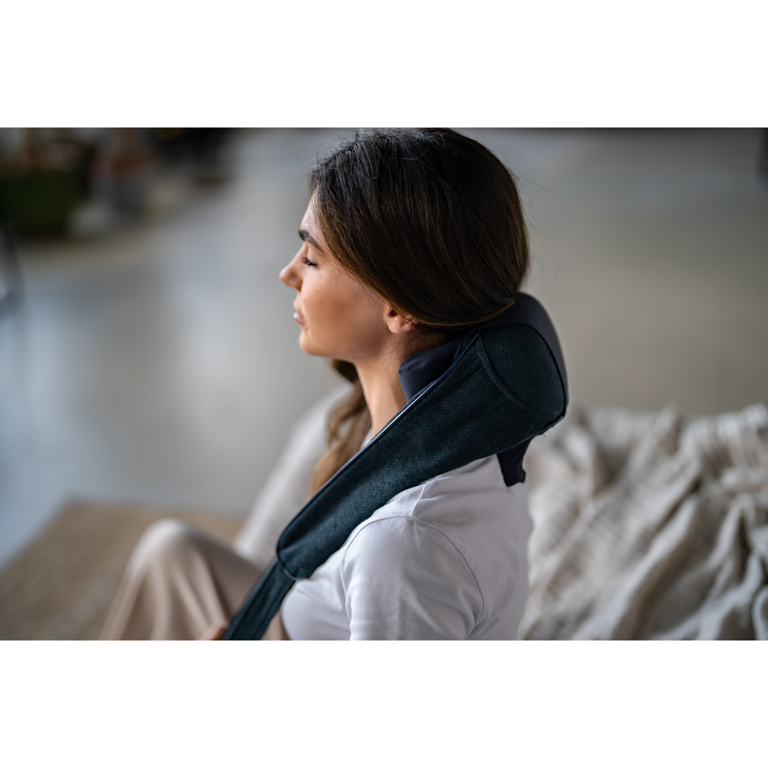 A woman rests with a neck massager. She closes her eyes. The background is an interior.