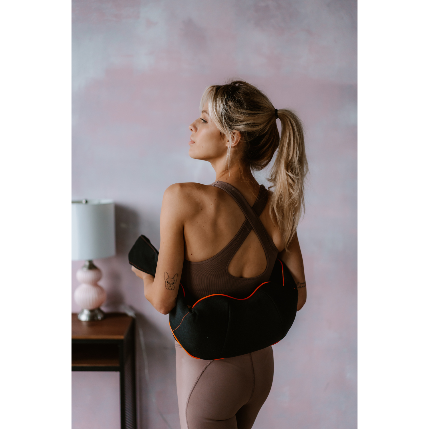 Vrouw in sportkleding, met een zwart massage-instrument, kijkt weg.