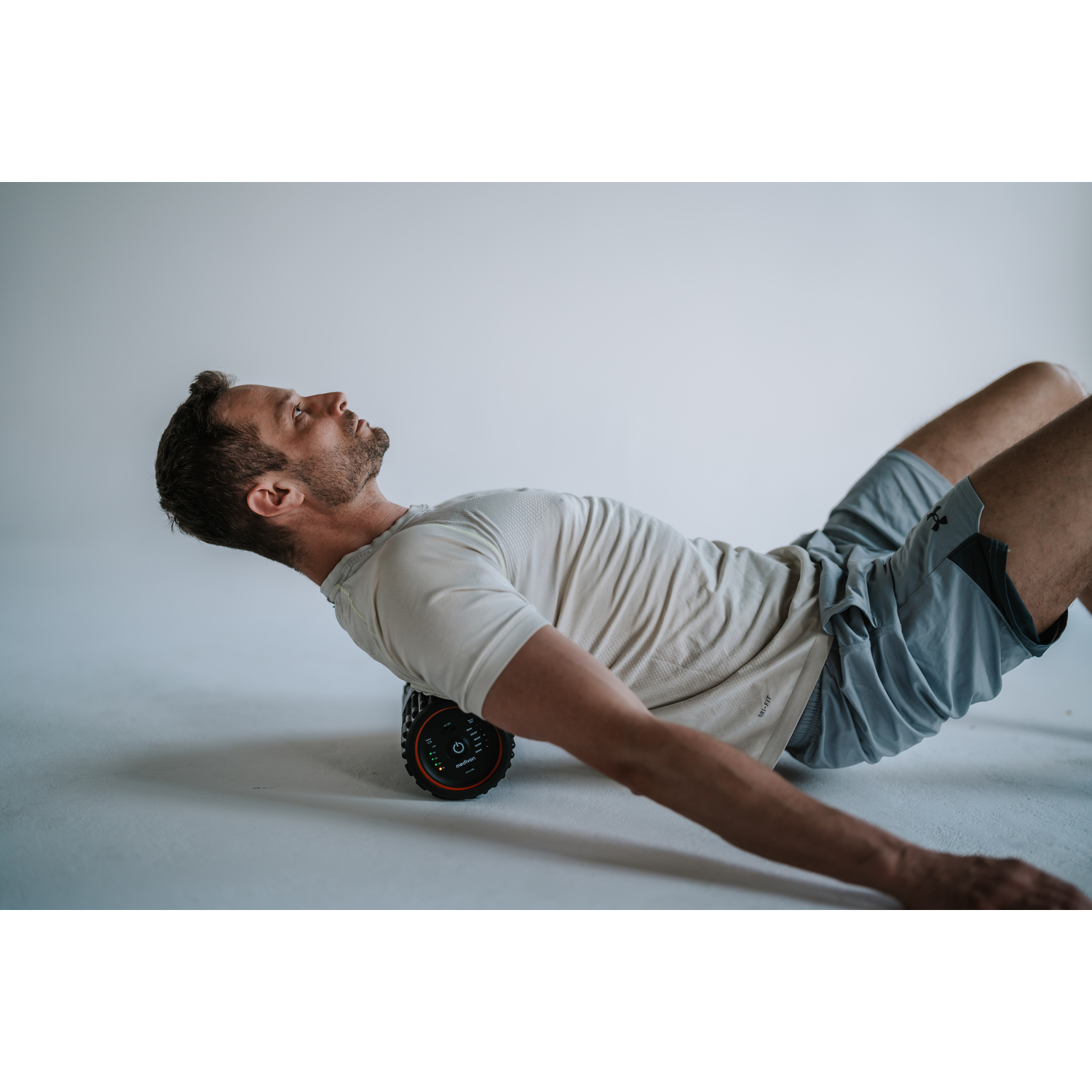 Man on roller. He is stretching. Black and orange roller.