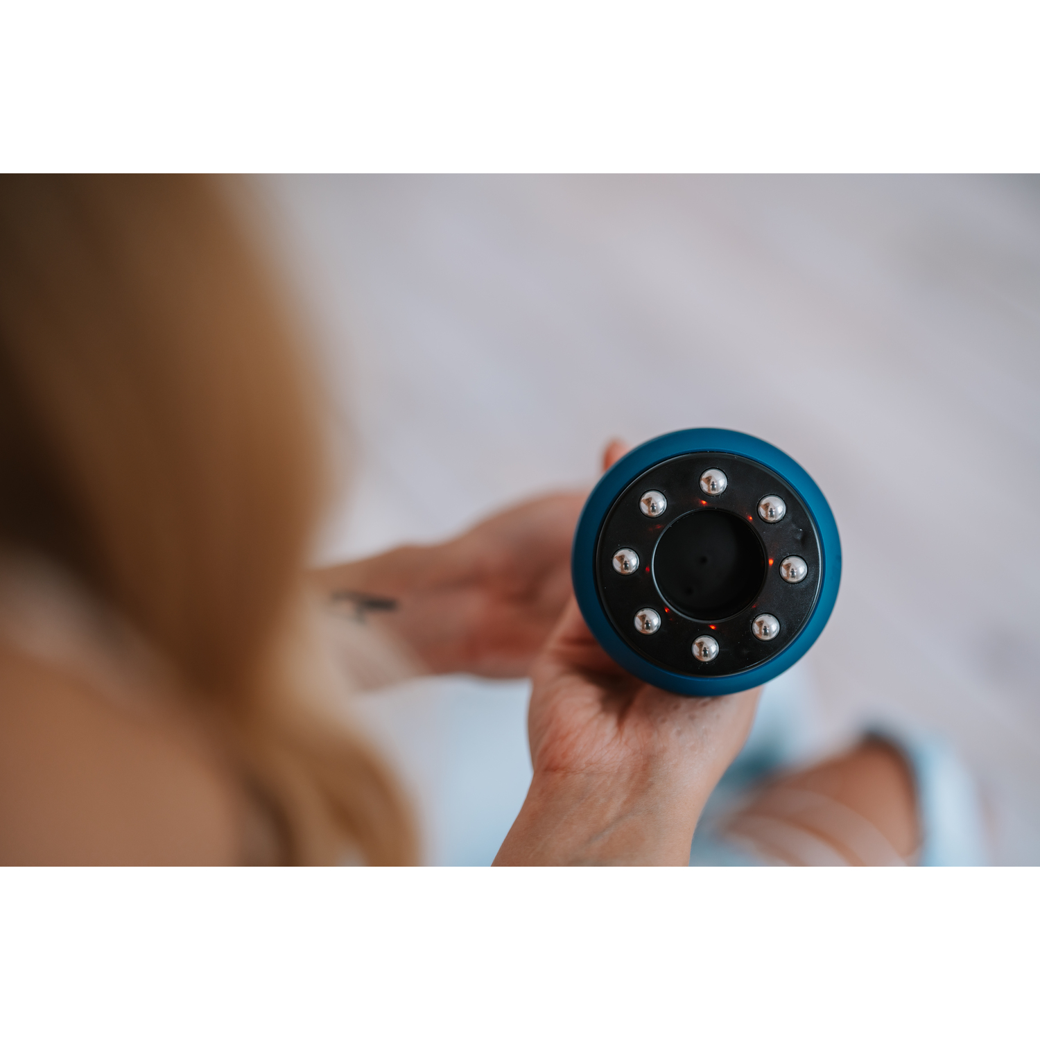 Woman holding a blue massage device. Focus on device and hands. Light wood surface.