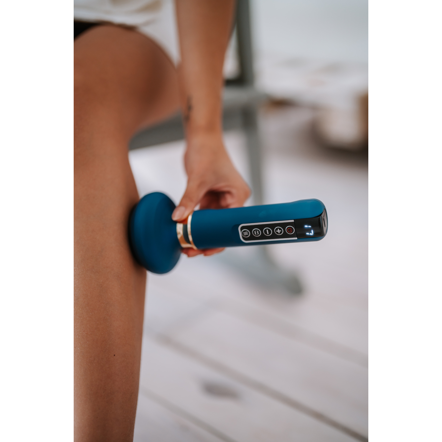 Person using a blue massage device on leg. Light wood surface. Hand holding the device.