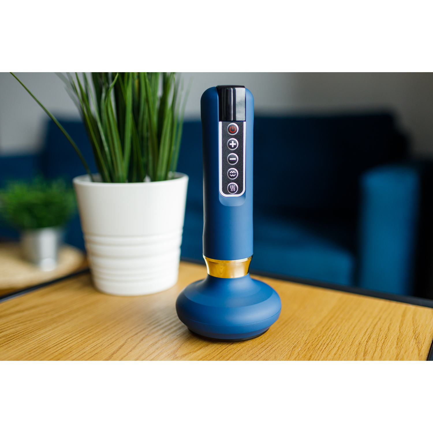 Blue and gold massage device on a wooden table with a plant and sofa in the background.