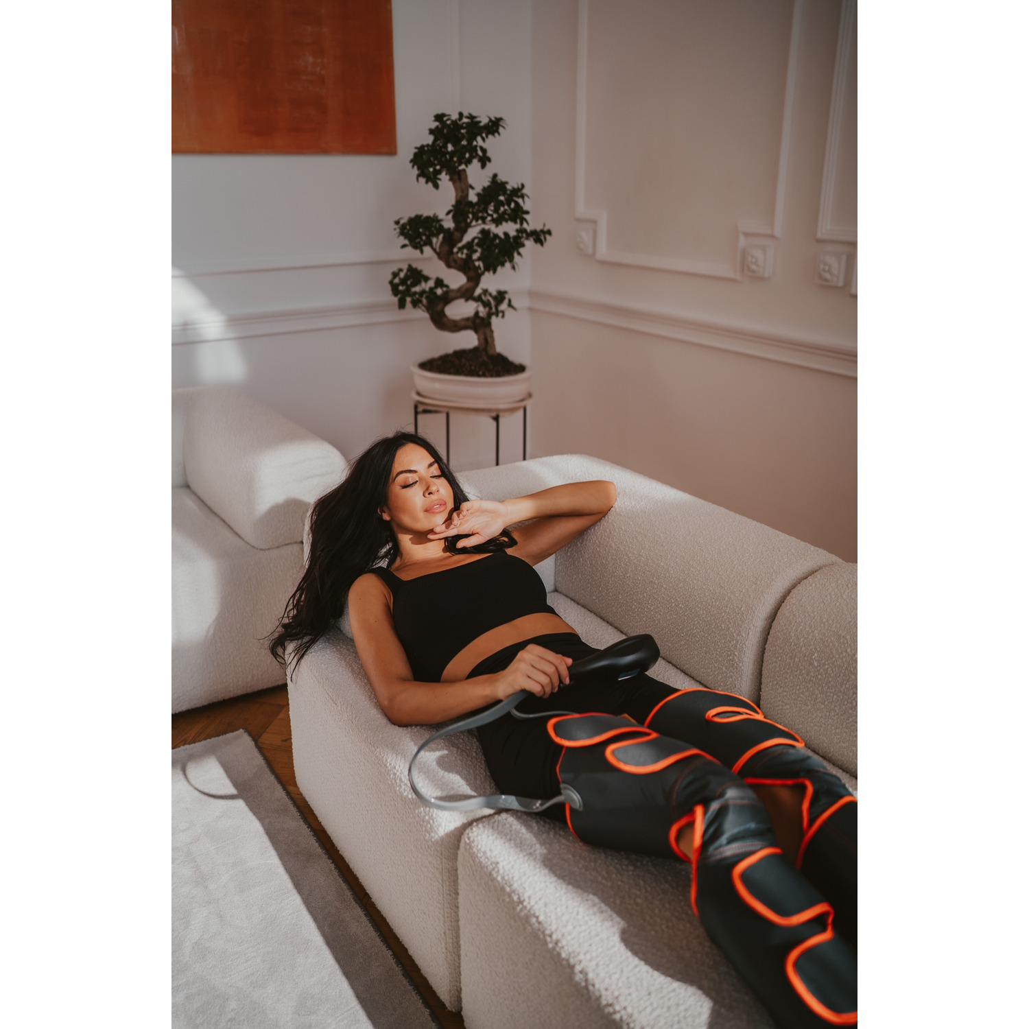 Woman lying on a couch using leg massager with red lights.