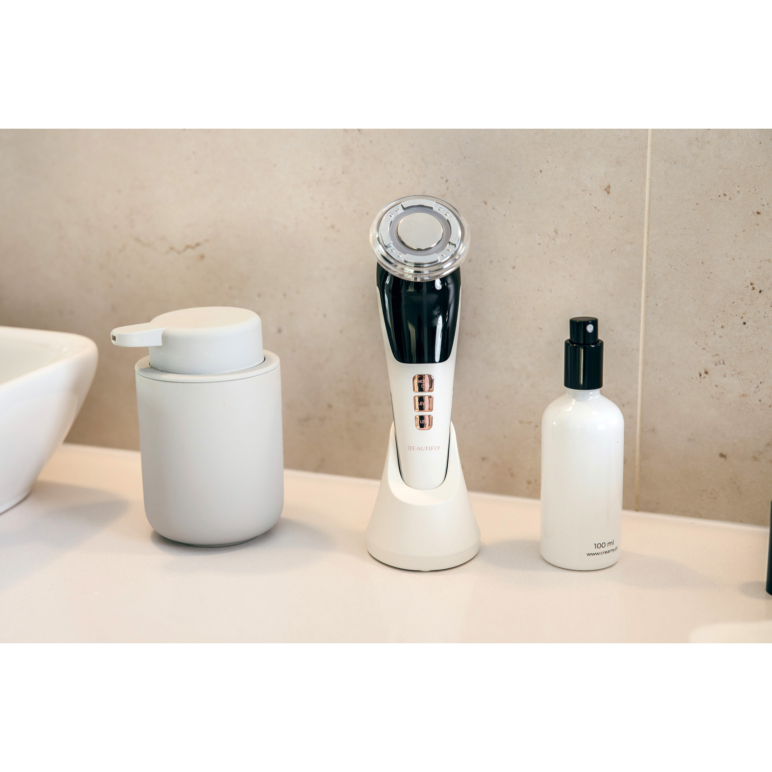 A white countertop with skincare devices, a soap dispenser, and a spray bottle.