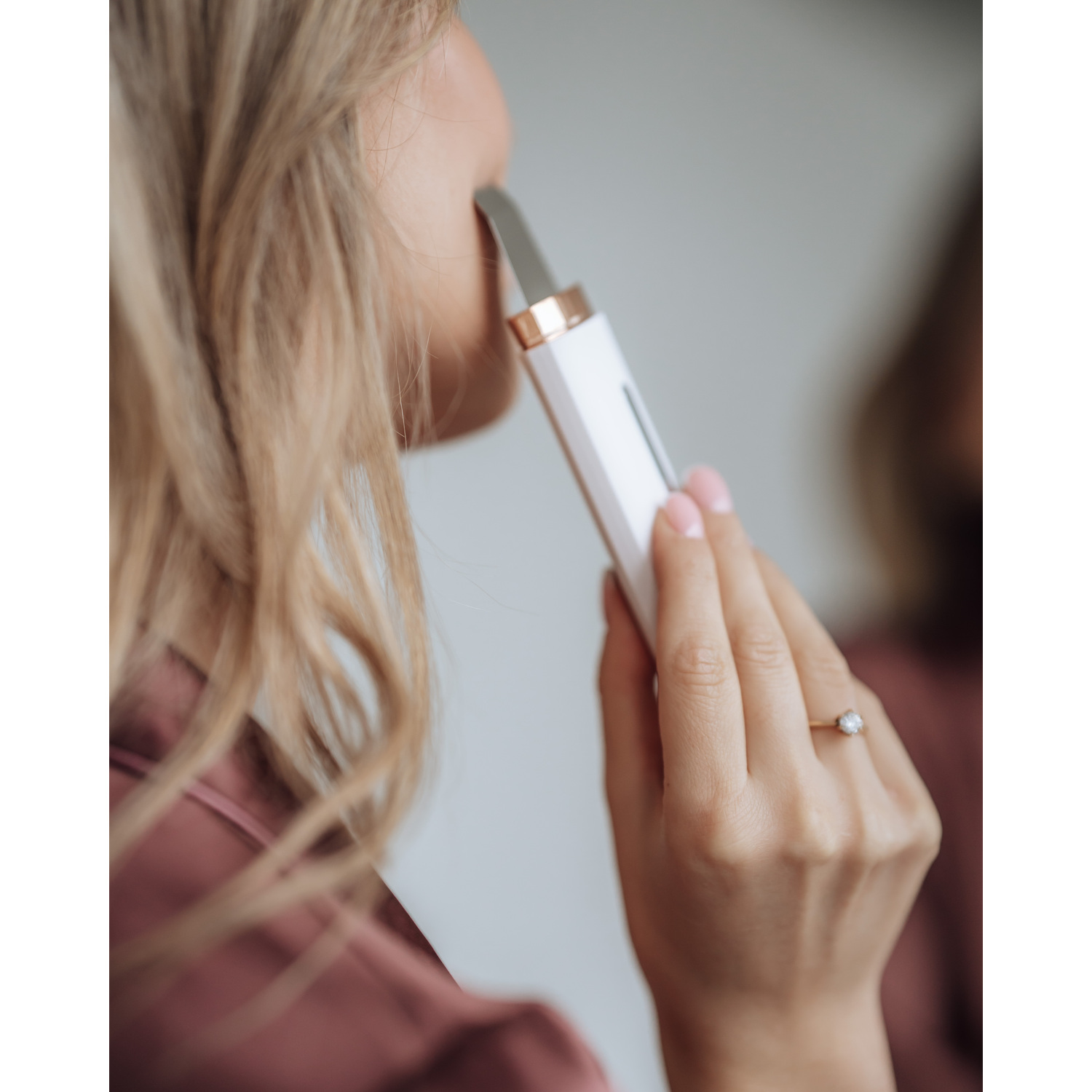Femme utilisant un appareil de soin de la peau sur son visage, près d'un miroir.
