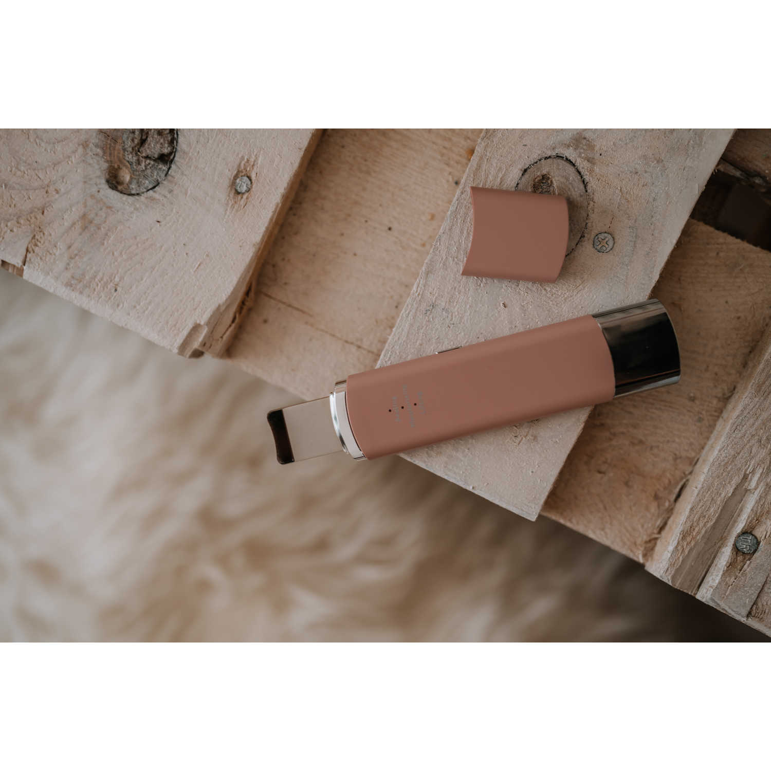 A pink facial cleansing device rests on wood. A lid is beside it.