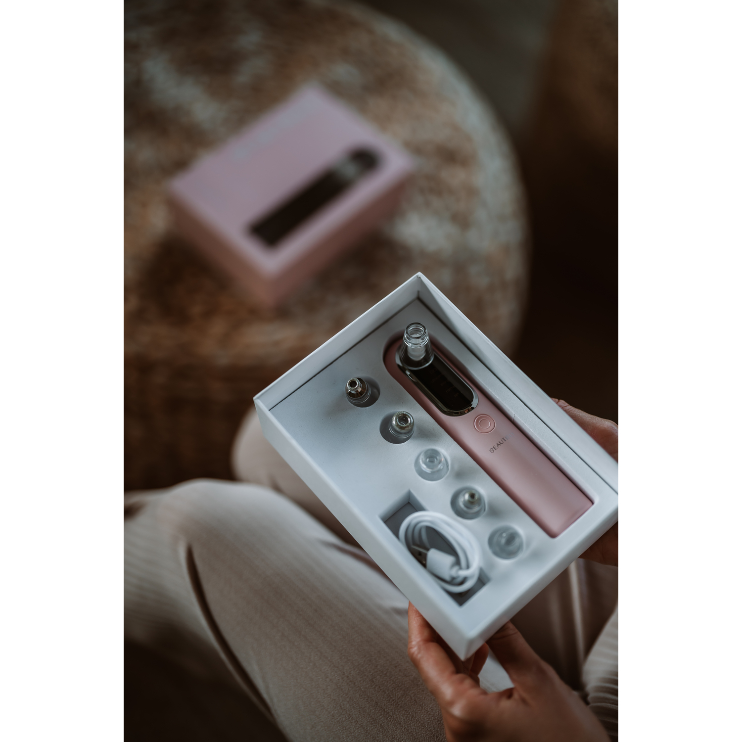 Woman holding open box with pink beauty device and accessories. 