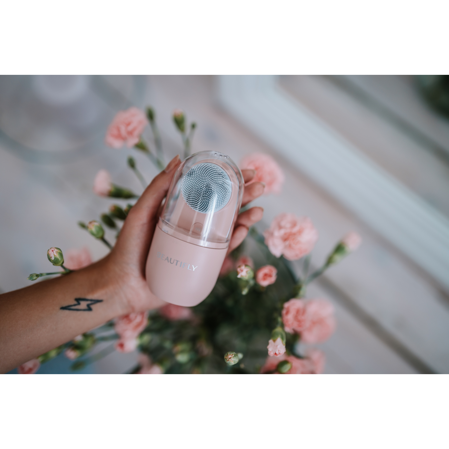 Person holding a pink Beautifly facial cleansing brush.