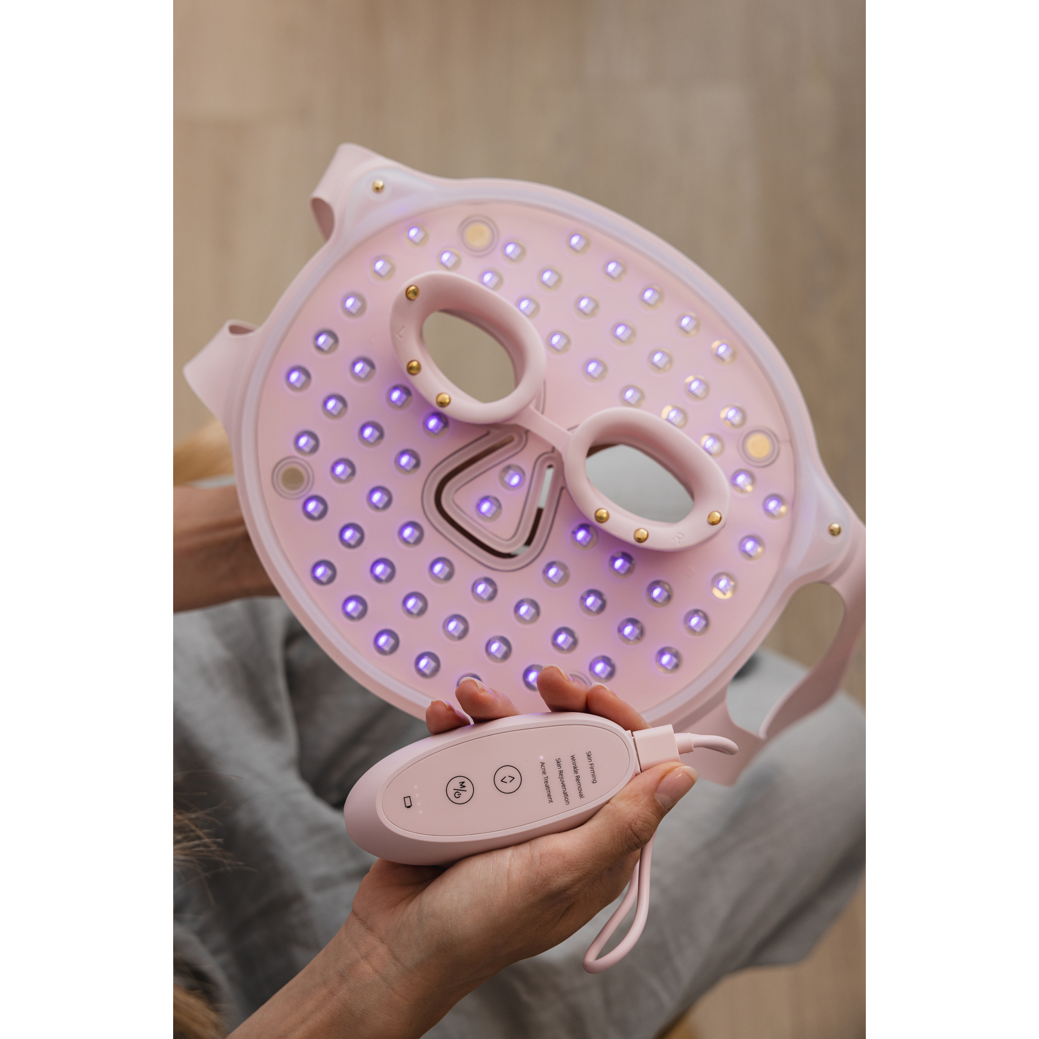 Person holding a pink face mask with lights and remote control. 