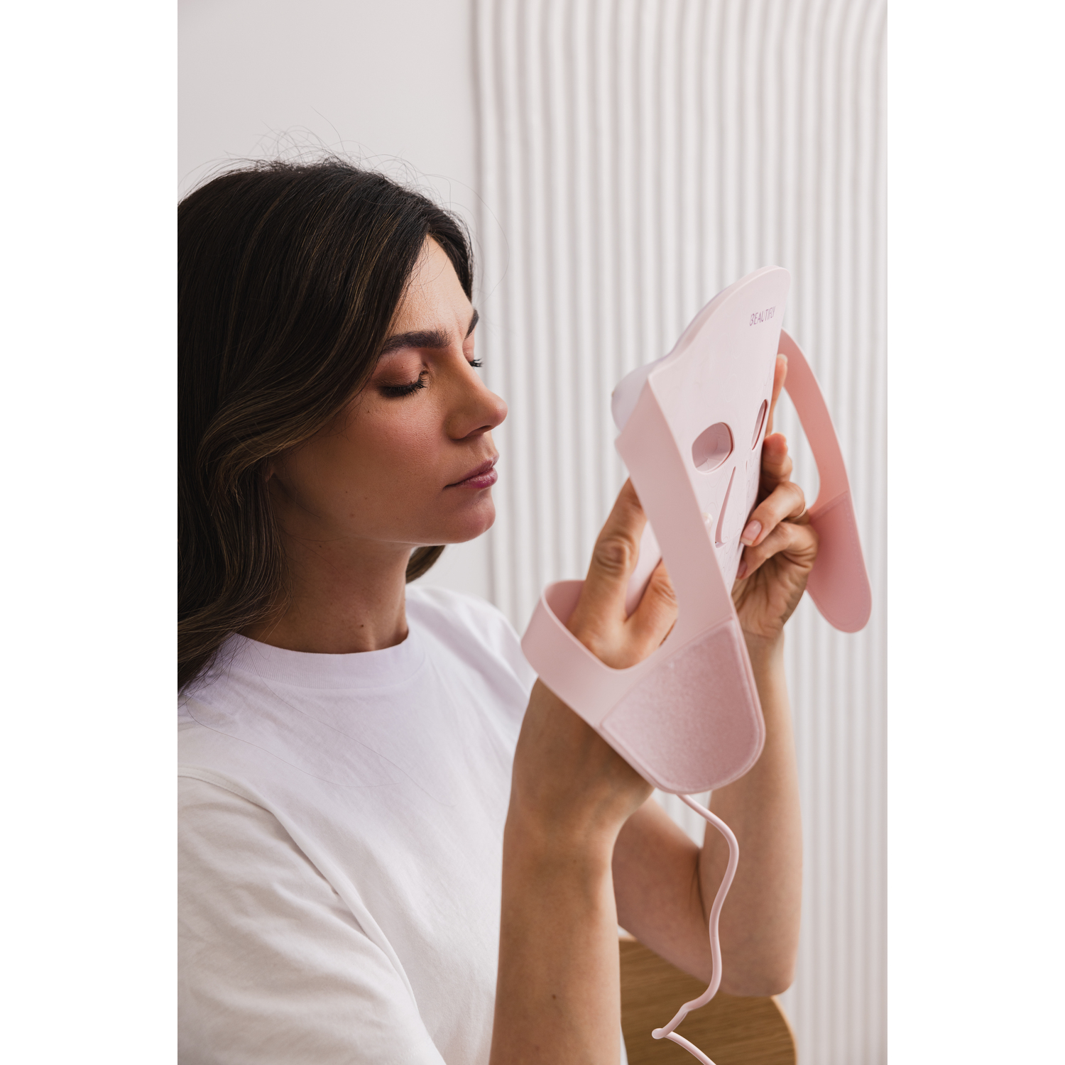 Woman holding a pink beauty device mask, looking at it closely.