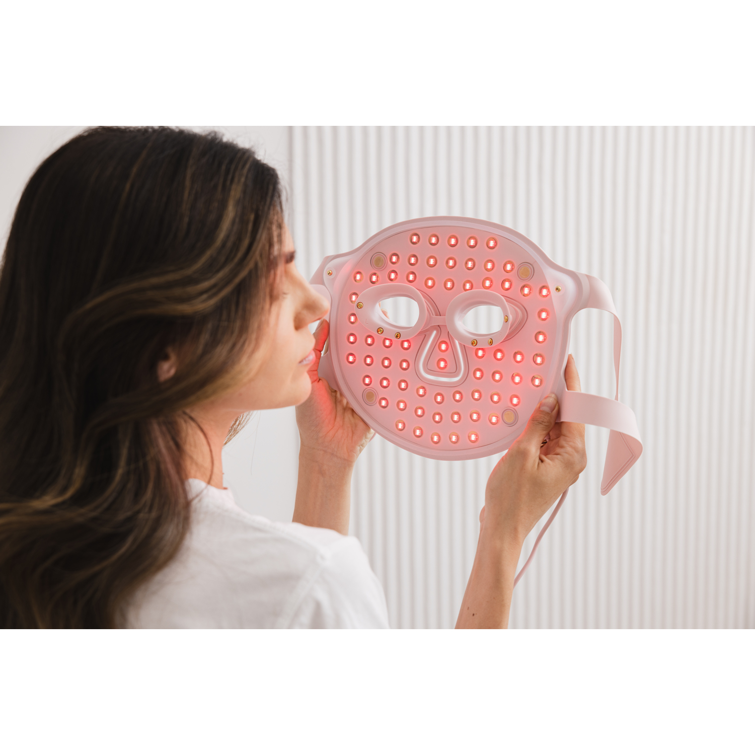 Woman holding pink face mask with lights, looking at it. 