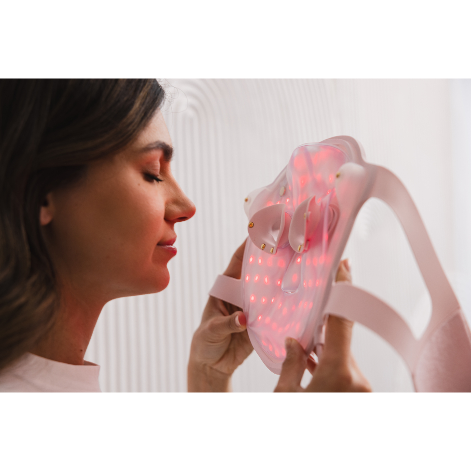 Woman looking at pink face mask with lights, close-up. 