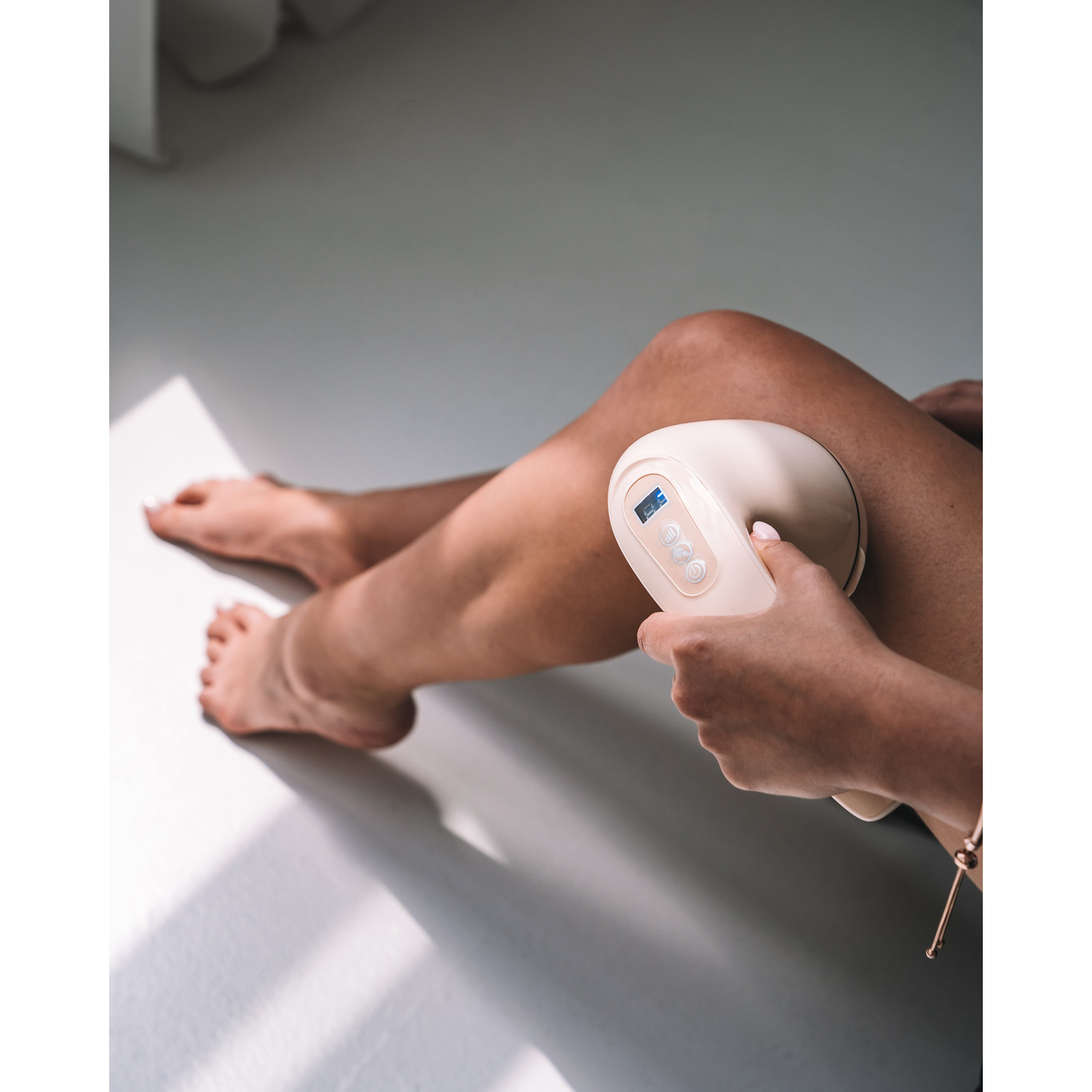 A woman massaging her leg with a beige massage device.