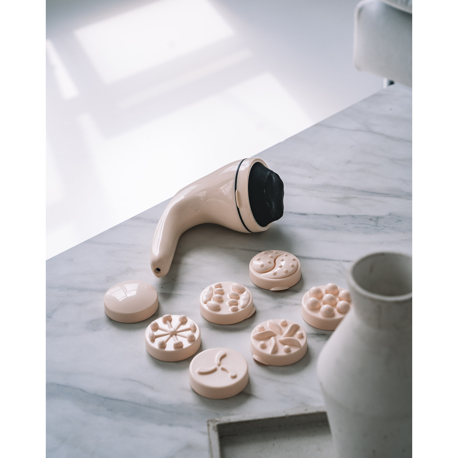 A beige massage device with several interchangeable attachments on a marble surface.