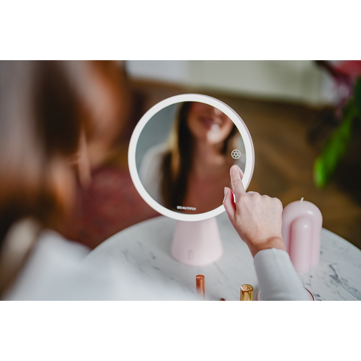 A woman's hand touching the illuminated mirror. Makeup items are on the table.