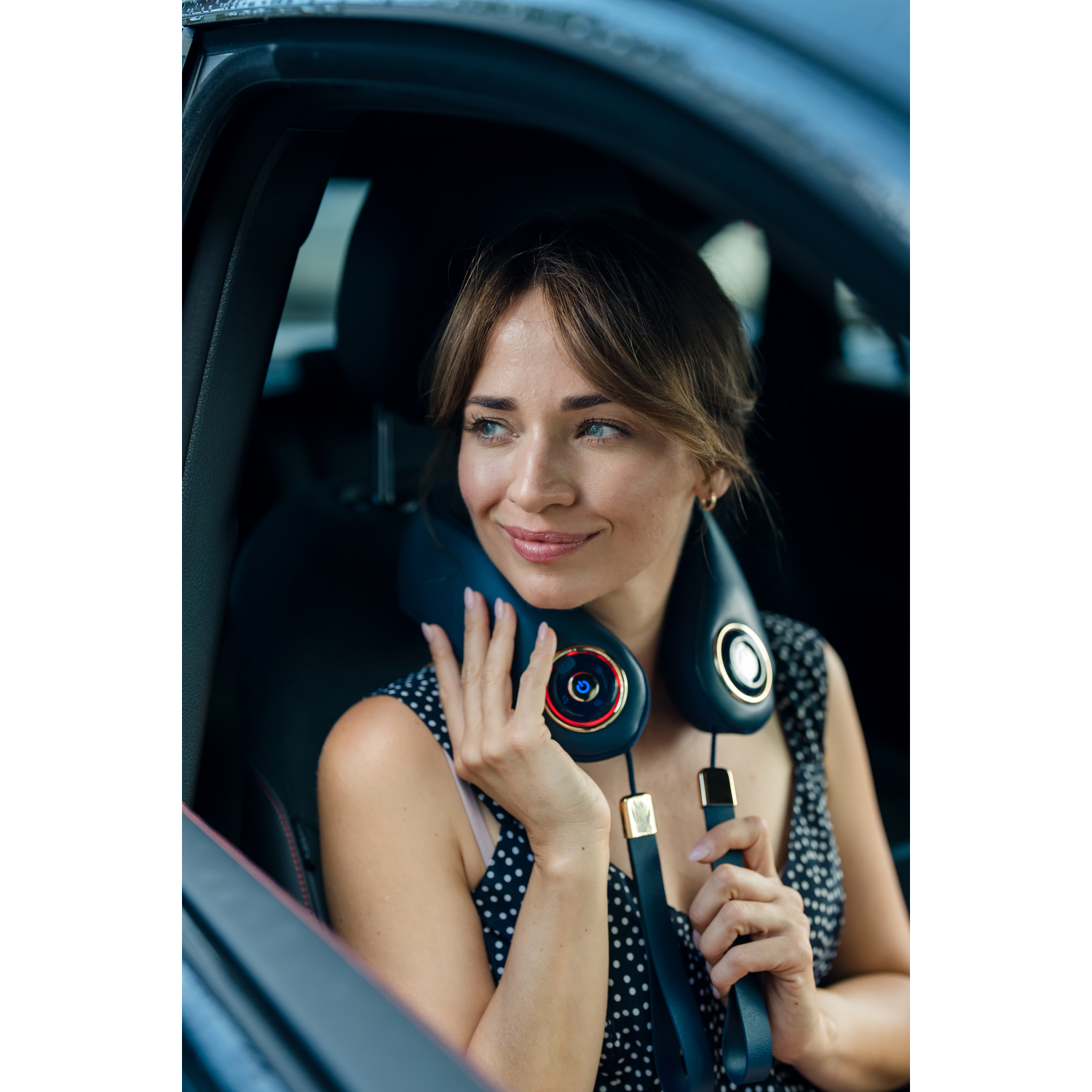 Woman in a car wearing a neck massager. She is smiling.