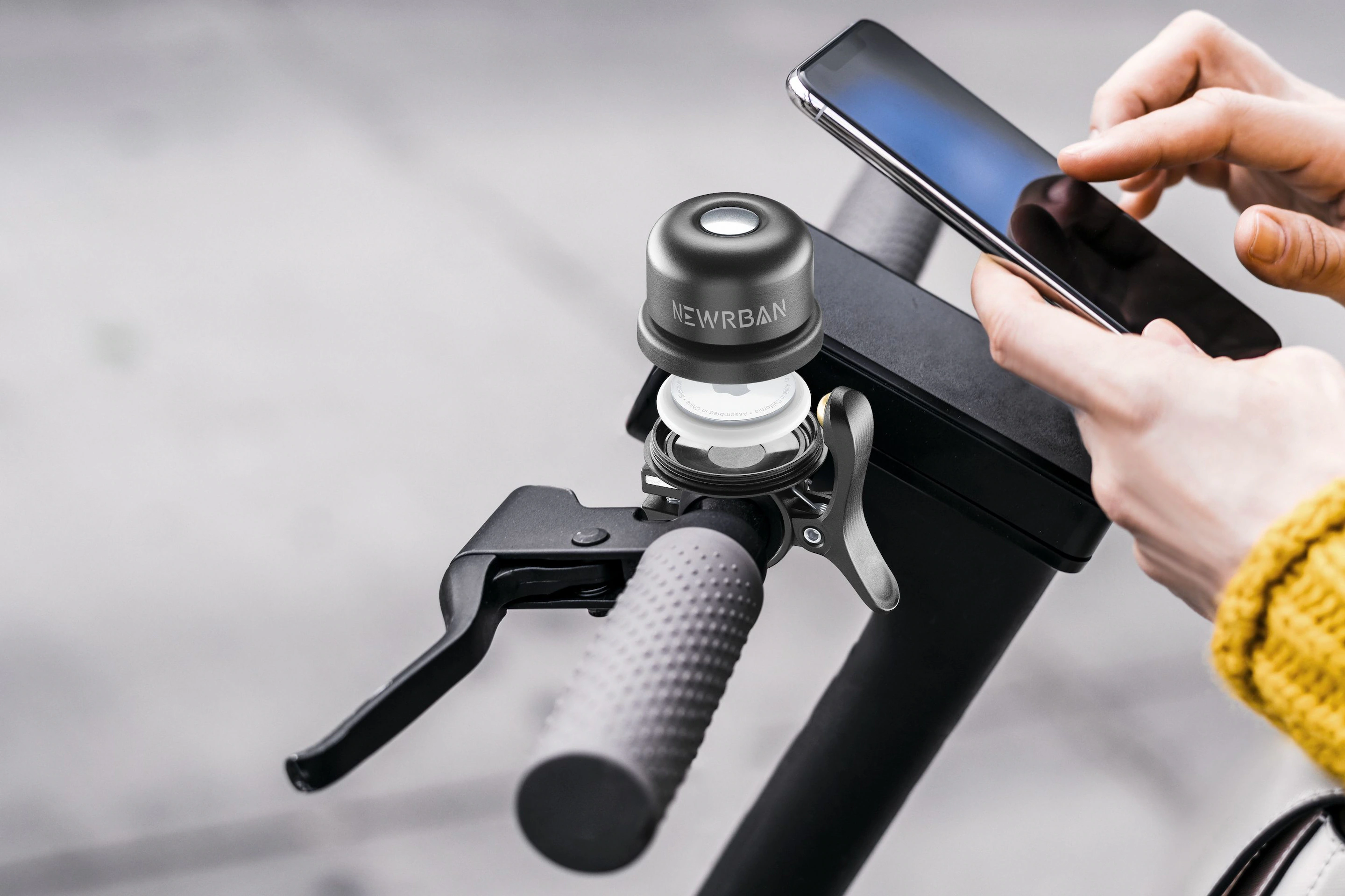Person nutzt Smartphone in der Nähe eines Rollerlenkers mit Klingel. Newrban Klingel am Lenker.