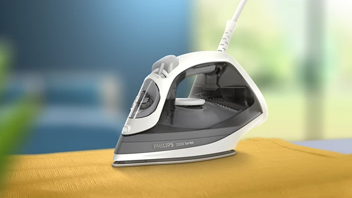 Ferro da stiro Philips bianco e grigio su tessuto giallo. Lo sfondo è sfocato con blu e verde.