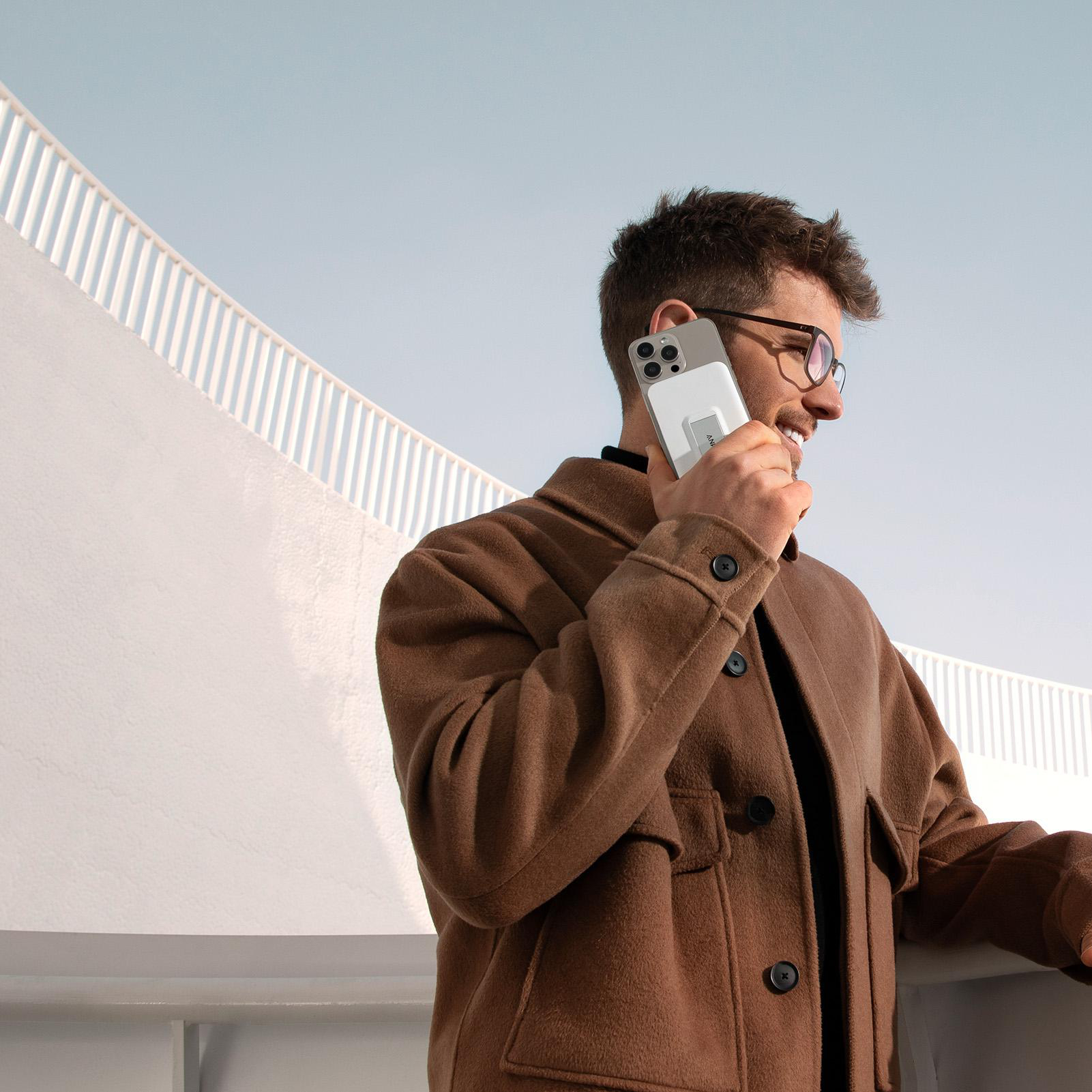 Mann, der ein Telefon benutzt, trägt eine braune Jacke, vor weißem Hintergrund.