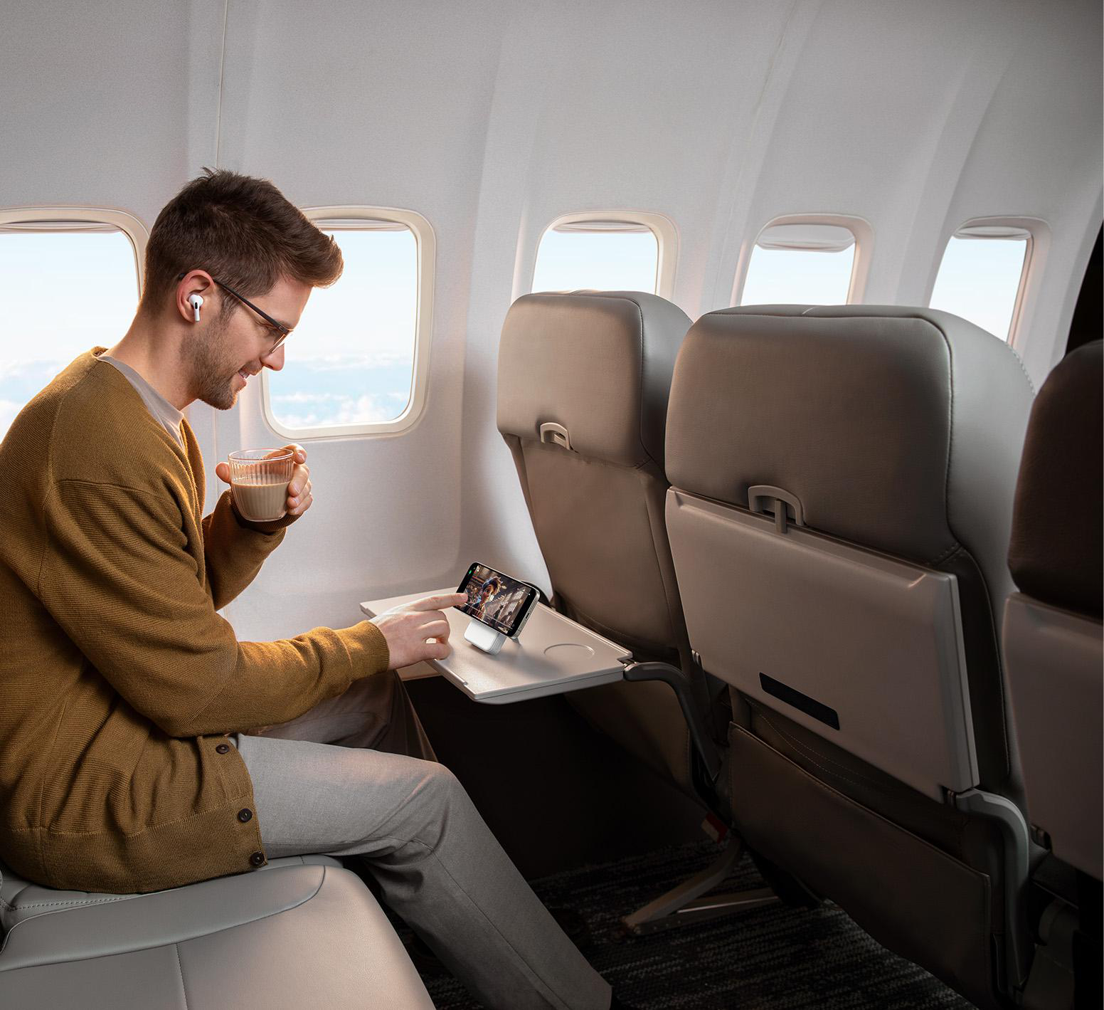Mann im Flugzeug benutzt Telefon auf einem Tisch, trinkt Kaffee.