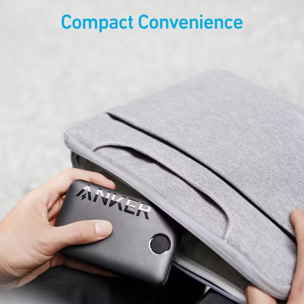 Eine Hand, die eine schwarze Anker Powerbank in eine graue Laptop-Hülle legt.