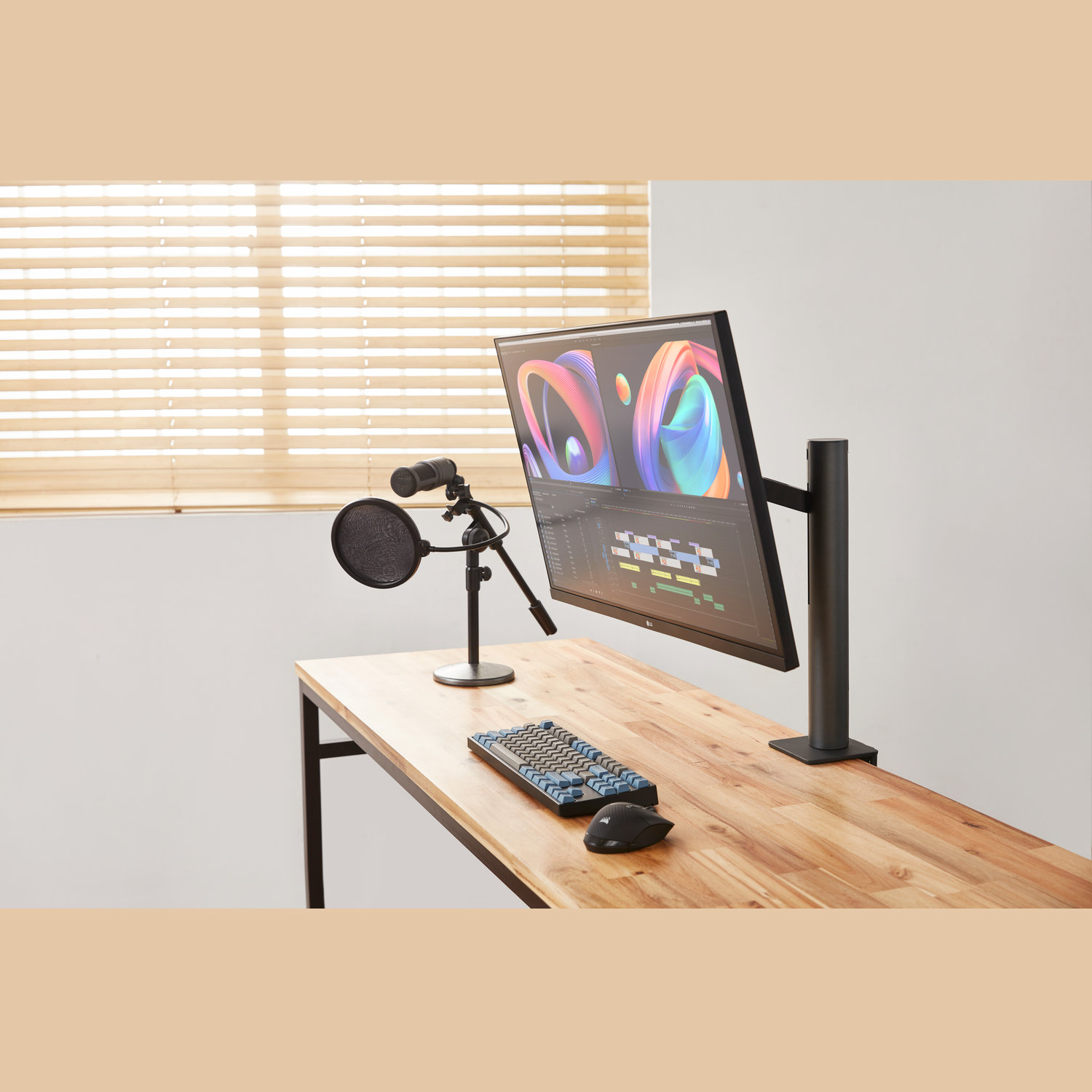 Een werkplek met een monitor met bewerkingssoftware, microfoon, toetsenbord en muis op een houten bureau. Raam met jaloezieën.