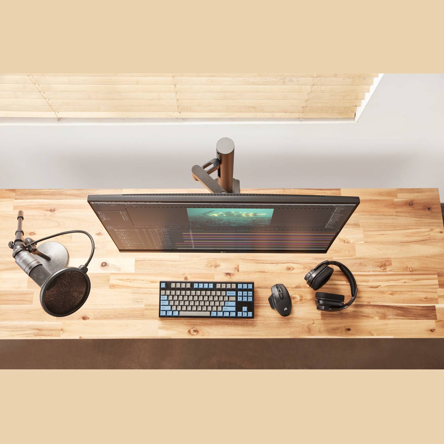Bureau-opstelling met monitor, toetsenbord, muis, koptelefoon en microfoon op houten oppervlak. Een raam erboven.