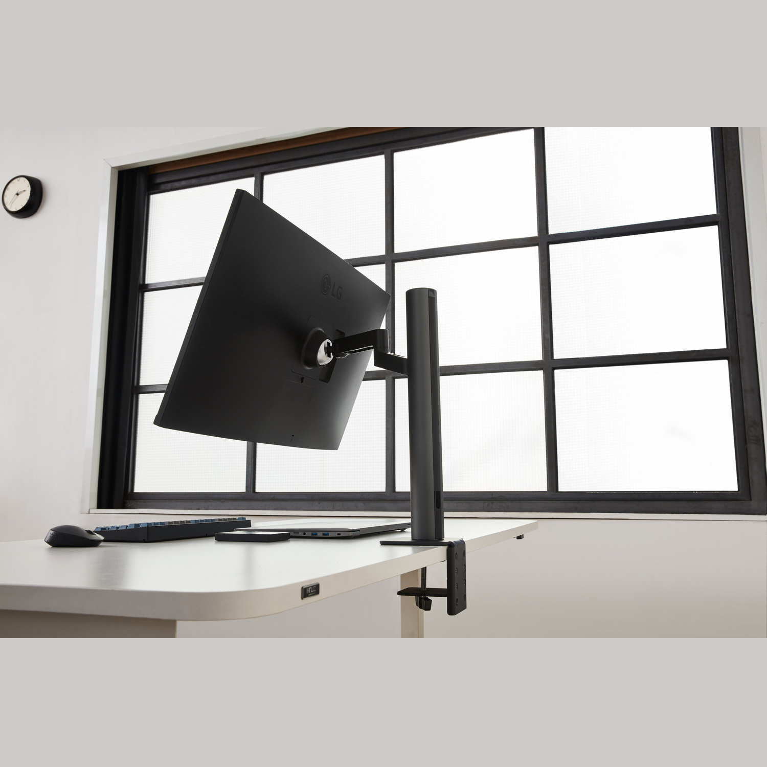 Een zwarte computermonitor is op een witte bureau gemonteerd. Een raam is op de achtergrond.