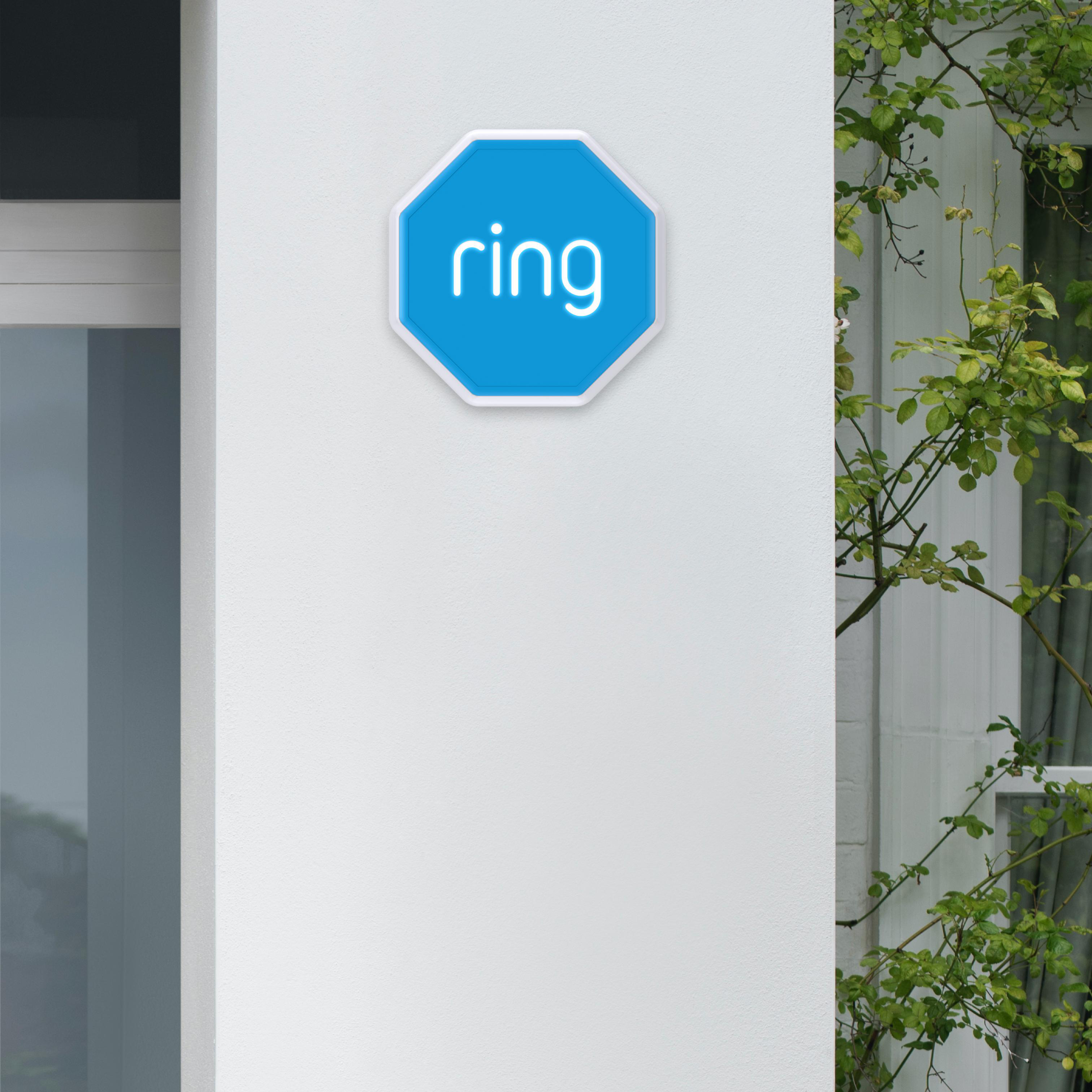 Ein blaues Ring-Sicherheitsschild an einer weißen Wand. Grüne Blätter sind im Hintergrund.