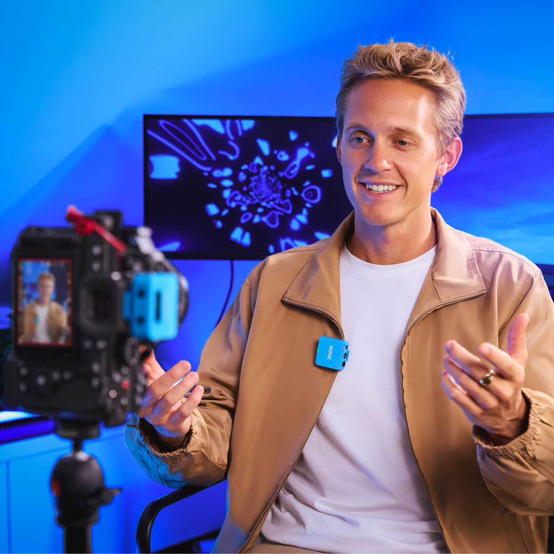 Homme faisant un vlog avec une caméra et un microphone bleu, avec un fond bleu.