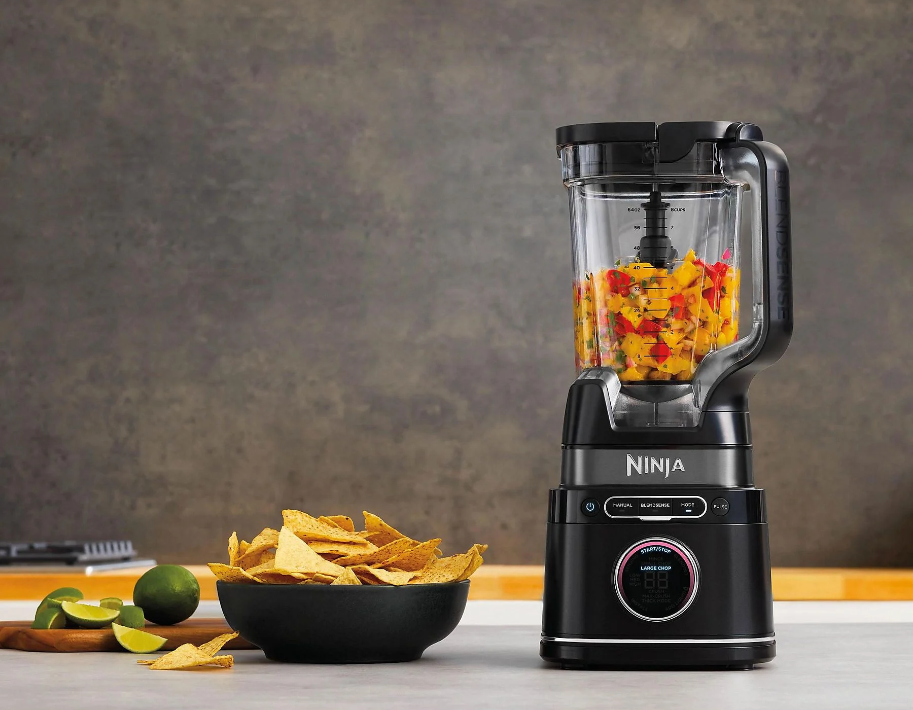 Egy fekete Ninja turmixgép gyümölccsel. Tortilla chips és limetta van mellette.