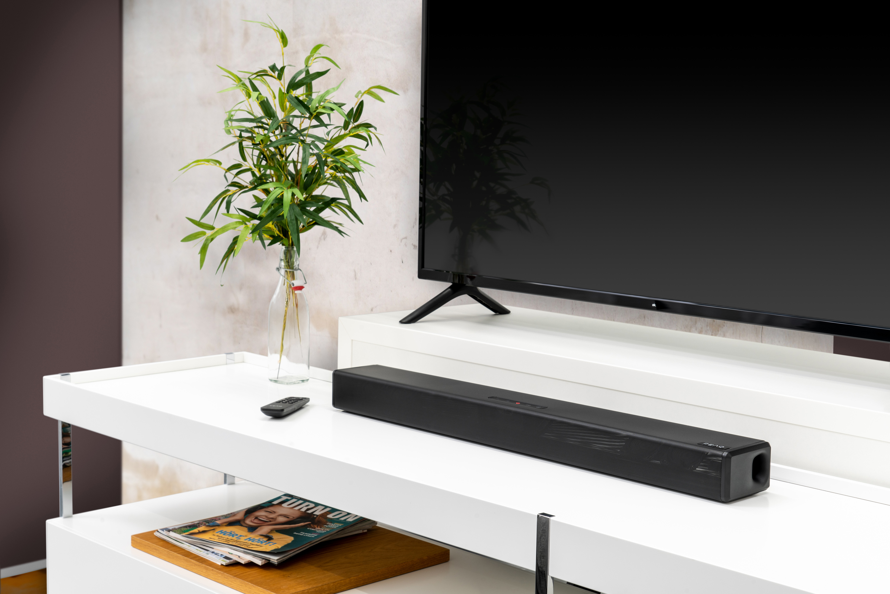 Barre de son noire, TV, plante, table blanche.