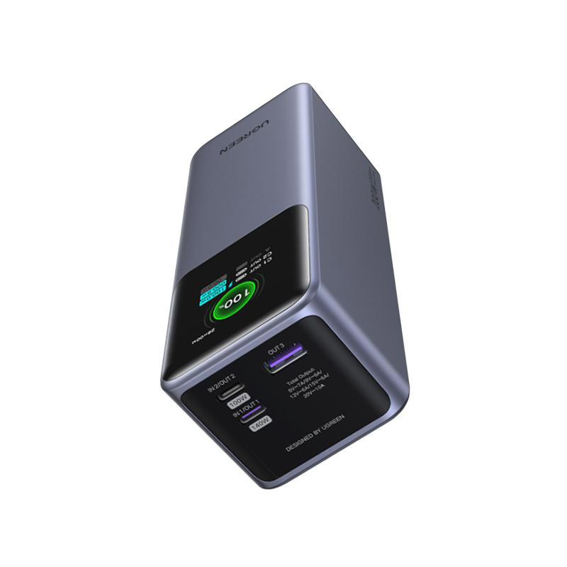 Dunkelgraue UGREEN Powerbank mit Anzeige von 100%. Das Gerät befindet sich auf einer weißen Oberfläche.