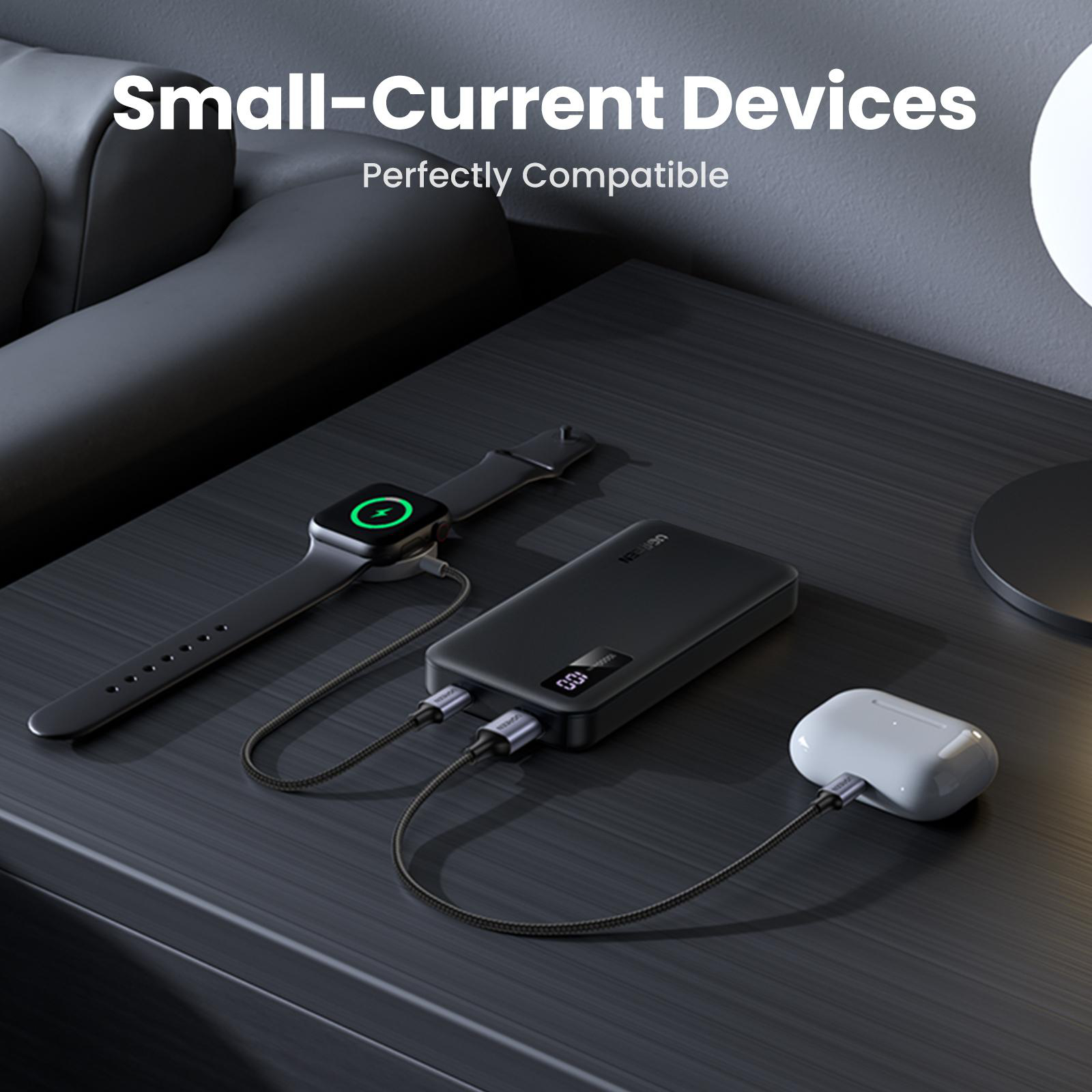 Schwarze Powerbank lädt Smartwatch und Ohrhörer auf dunkler Oberfläche.