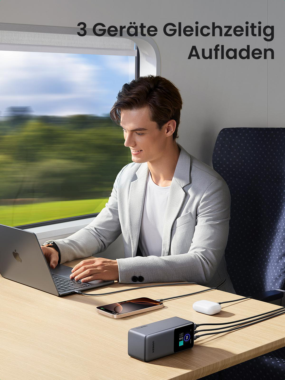 Mann benutzt Laptop im Zug, Ladekabel angeschlossen.