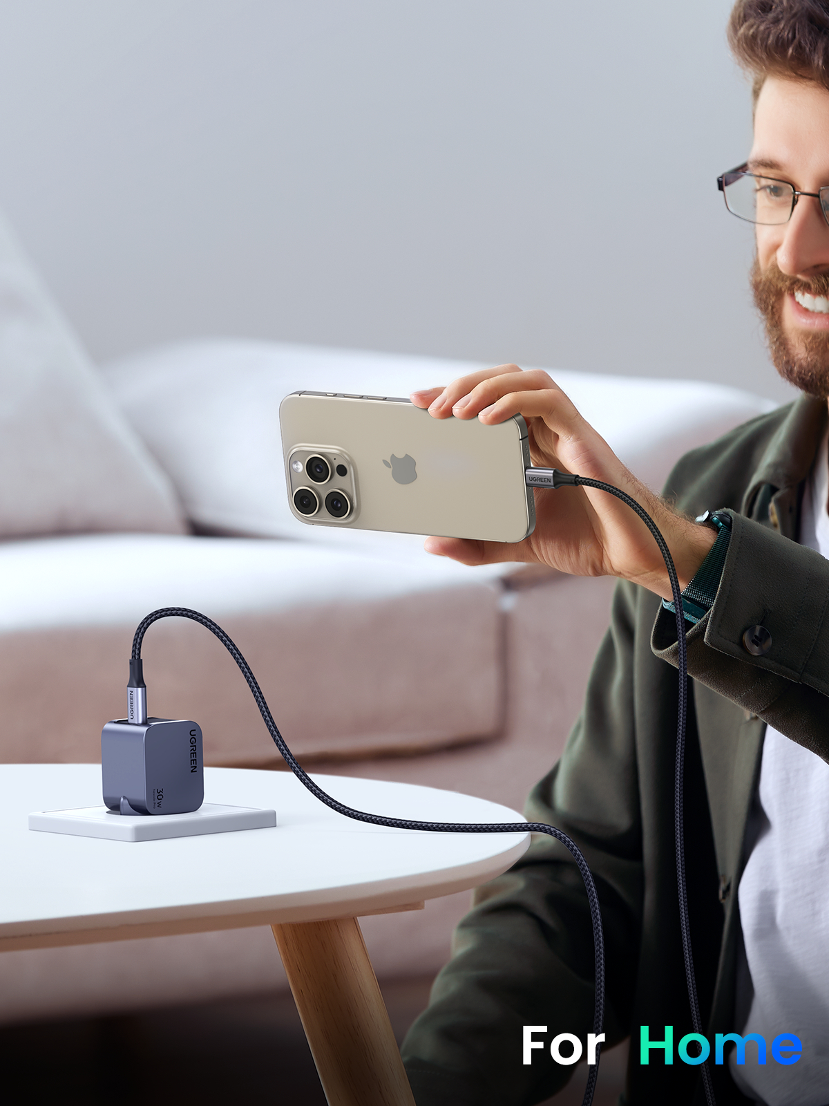 Mann hält ein Telefon, das mit einem UGREEN-Ladegerät geladen wird, auf einem Tisch.