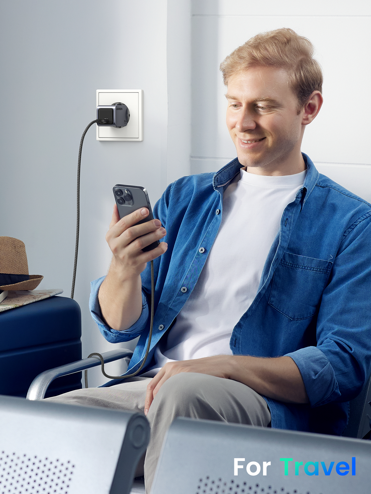 Mann, der ein Telefon mit einem UGREEN-Ladegerät in einem Raum verwendet, blauer Koffer im Hintergrund.