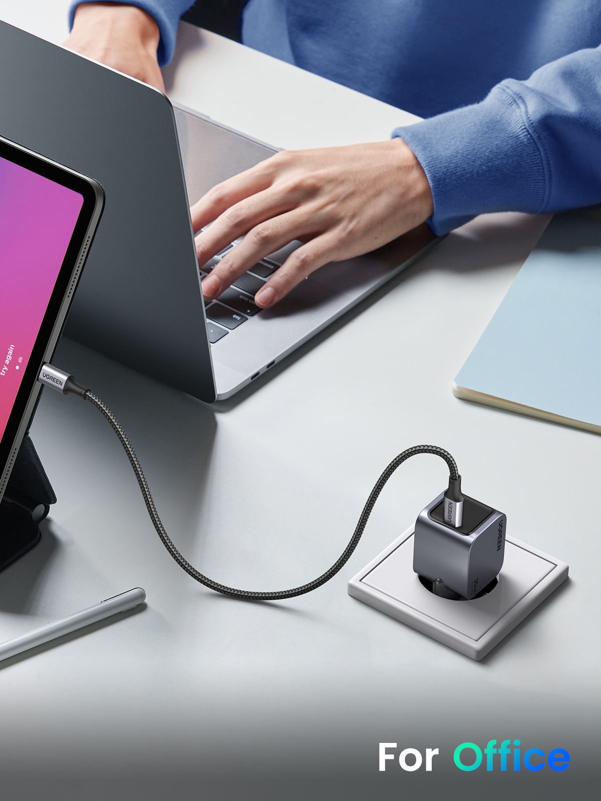 Eine Person arbeitet an einem Laptop und einem Tablet, mit eingestecktem Ladegerät.
