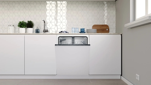 Un lavavajillas en una cocina blanca con la puerta abierta. Los platos están dentro, cocina limpia.