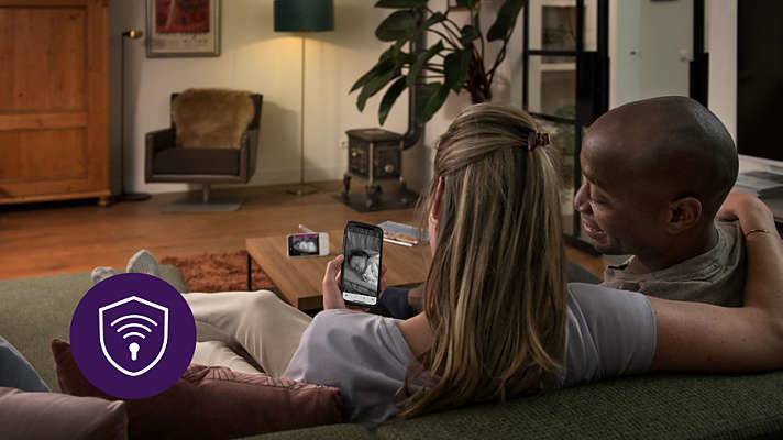 Paar schaut Baby auf Telefonbildschirm, sitzt auf Sofa.