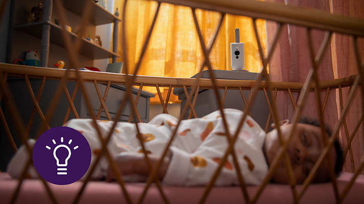 Baby schläft im Kinderbett, mit Babyphone im Hintergrund.