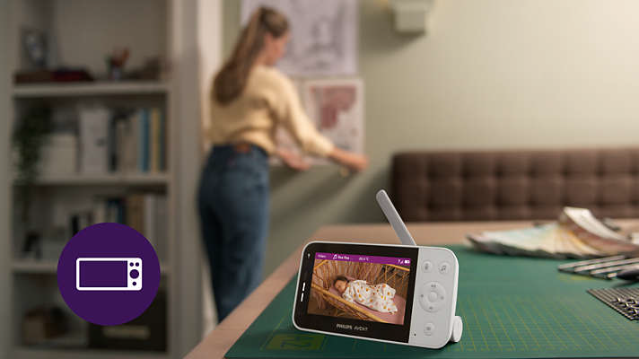 Babyphone, das ein Baby in einem Kinderbett zeigt, mit einer Frau im Hintergrund.