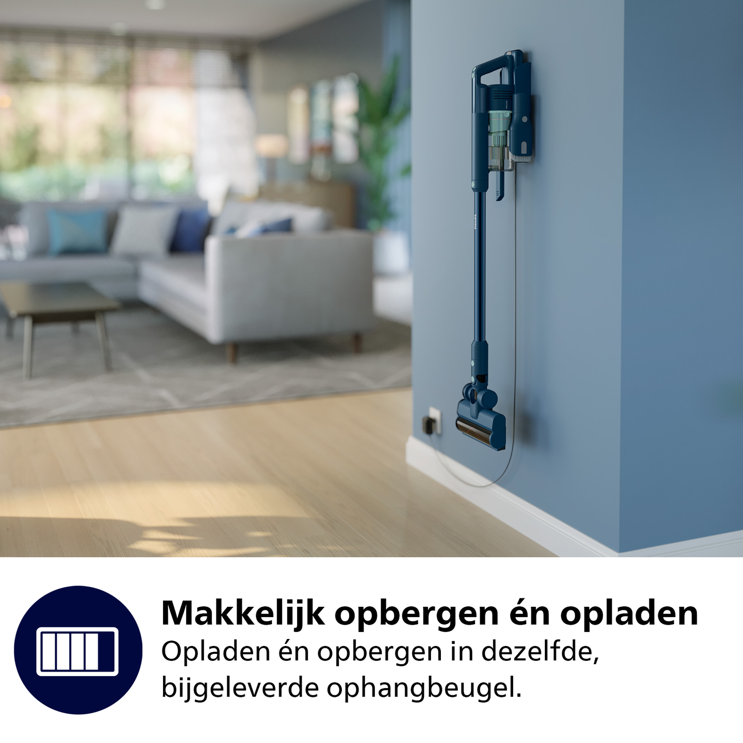 Een blauwe draadloze stofzuiger hangt aan een blauwe muur. Achtergrond: woonkamer met bank en houten vloer.