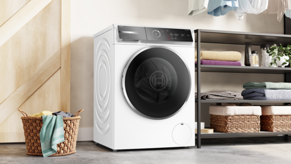 Beyaz bir Bosch çamaşır makinesi, bir çamaşır sepetinin yanında.