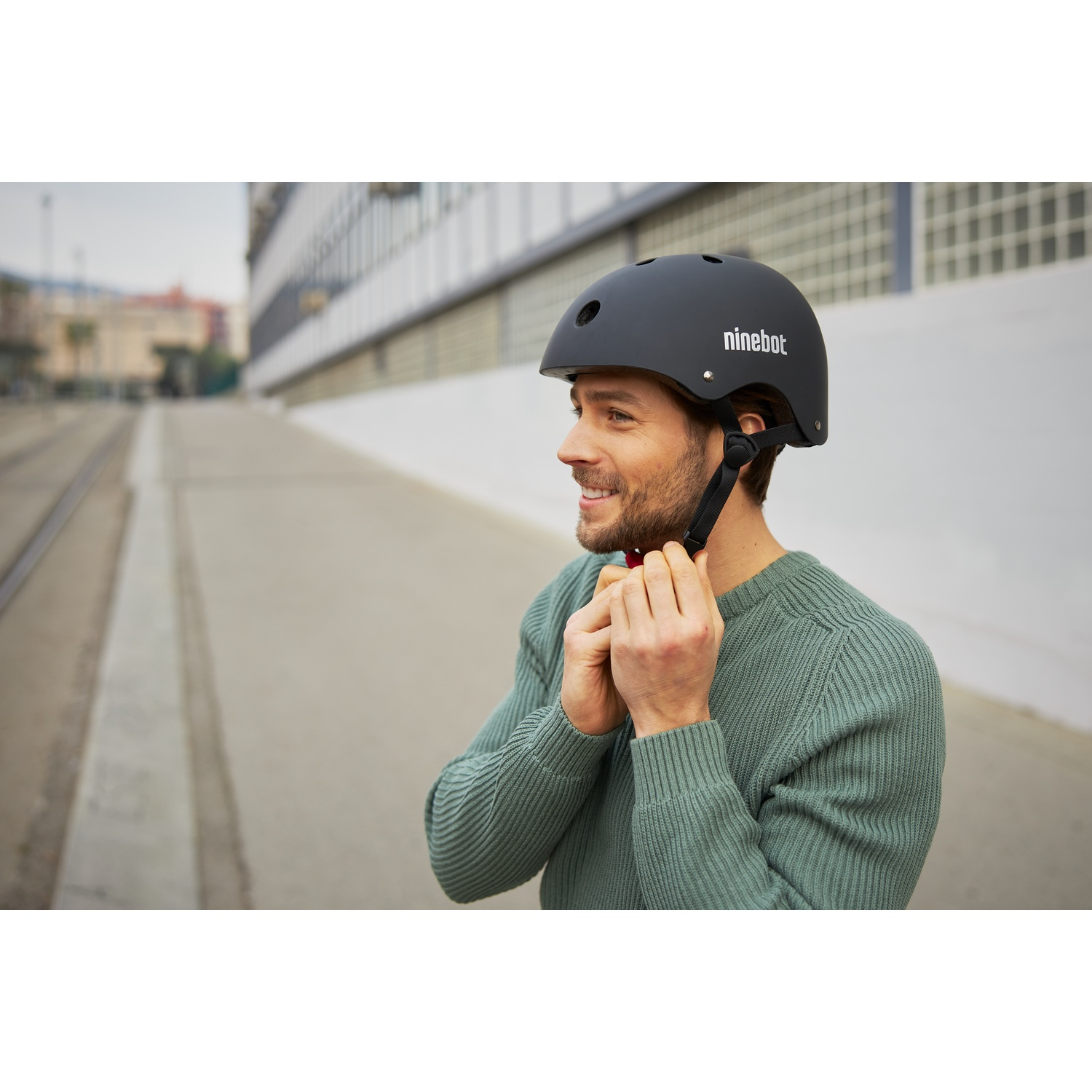 Uomo che regola il casco Ninebot nero, maglione verde, sfondo sfocato.